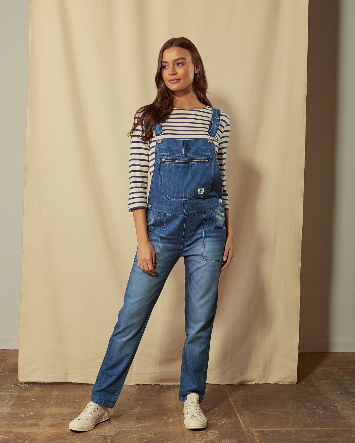 Front shot of women's washed organic denim bib-overalls with view of button closure, multiple pockets and adjustable straps.