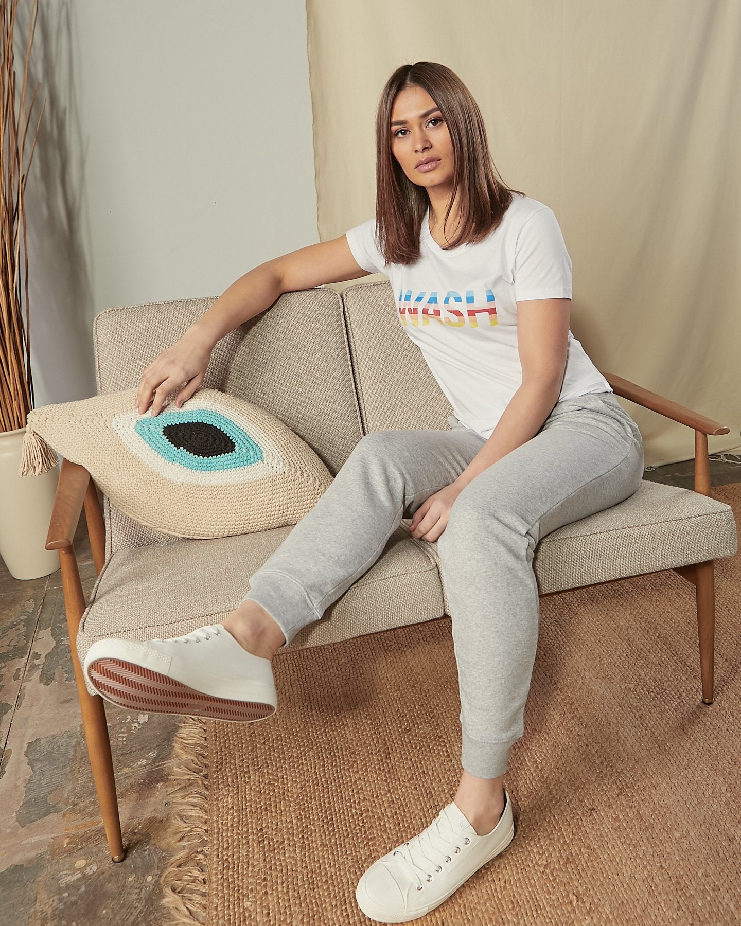Lounging on sofa wearing rainbow-coloured 'WASH' motif cotton t-shirt in white.
